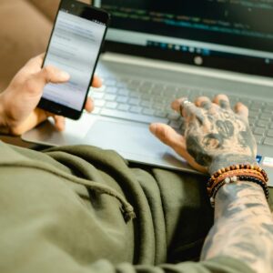 A focused individual coding on a laptop while checking a smartphone, embodying modern technology.
