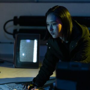 A woman working on a keyboard in a dimly lit room with tech equipment.