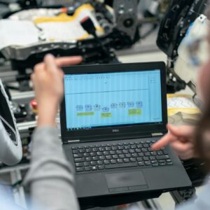 Engineers using a laptop to analyze software data in an industrial workshop setting.