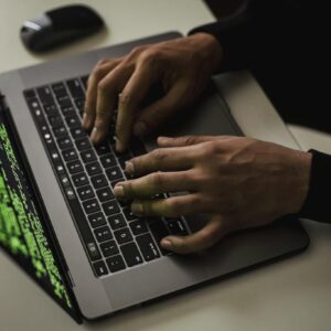 From above of crop anonymous male hacker typing on netbook with data on screen while sitting at desk