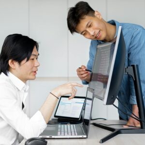 Two Asian men collaborating on a project using computers in an office.