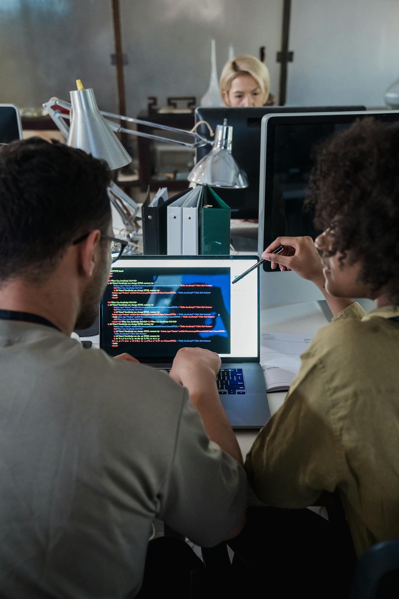 Two developers engage in software programming on a laptop in a modern office setting.